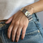 Person wearing a white tank top and blue jeans with multiple bracelets on a neutral background