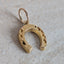 Gold horseshoe-shaped pendant on a light gray surface