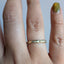 A close-up of a hand wearing a thin gold band ring with small clear stones set across the front, against a plain light background.