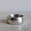 A wide, chunky sterling silver ring with a hammered, textured finish and a polished reflective center, resting on a light beige stone surface.