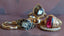 A group of vintage-style gold rings with various gemstones and engravings, displayed on a textured mauve-brown background.