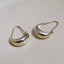 A pair of polished silver crescent-shaped hoop earrings with leverback closures, displayed on a neutral beige surface.