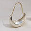 A silver crescent-shaped earring with a gold-colored wire ear loop, displayed on a neutral light gray surface.