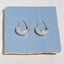 Pair of silver hoop earrings on a blue card against a white background