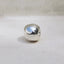 A single polished silver bead charm with a reflective metallic surface, resting on a light beige textured surface.
