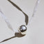 Necklace with a silver bead on a white cord against a beige background